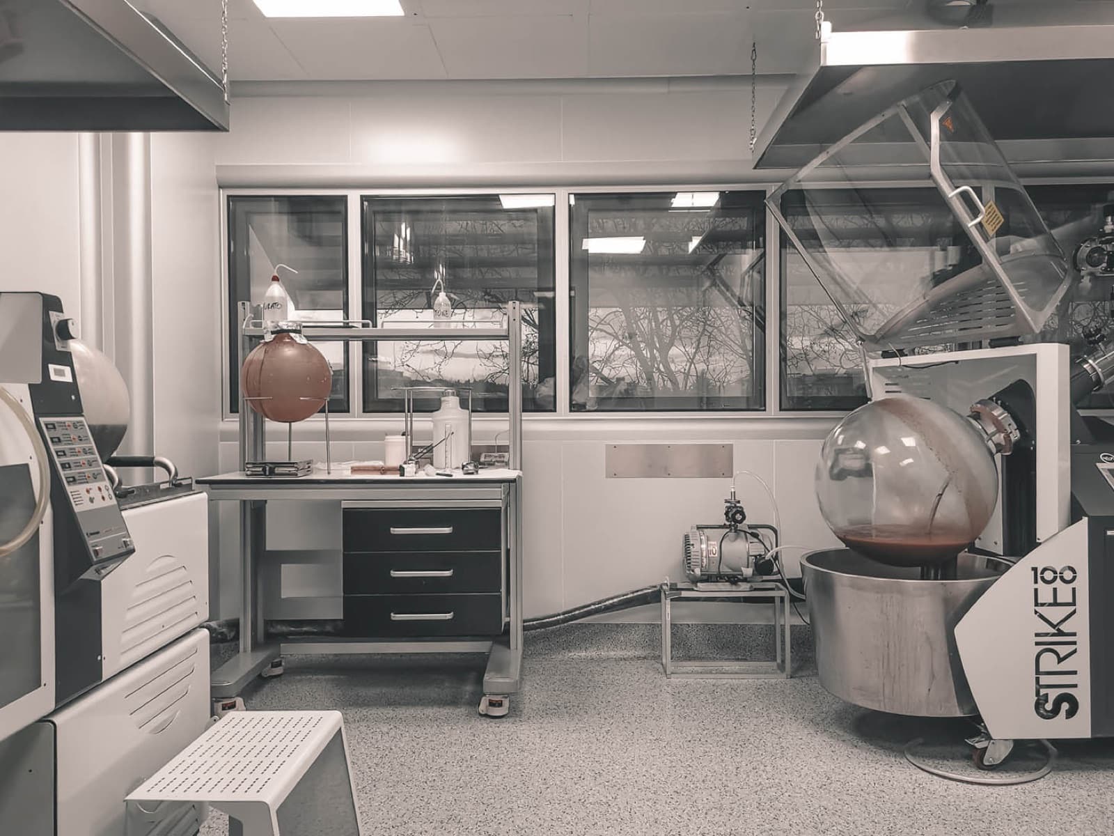 Banco di laboratorio per il controllo qualità, con vetreria borosilicata e bilancia analitica di precisione sotto la cappa di protezione